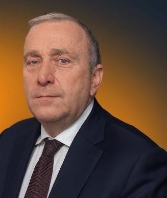 Grzegorz Schetyna przemawiający na wiecu lub konferencji prasowej, wykonujący gesty ręką, z rozmytym tłem sugerującym tłum lub symbole polityczne.