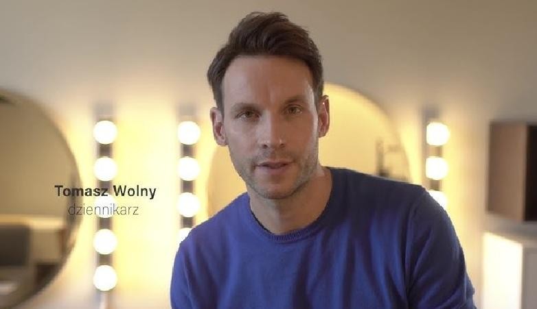 Tomasz Wolny uśmiecha się, ukazując swoją charyzmę, z subtelnymi elementami tła nawiązującymi do jego życia prywatnego lub pasji.