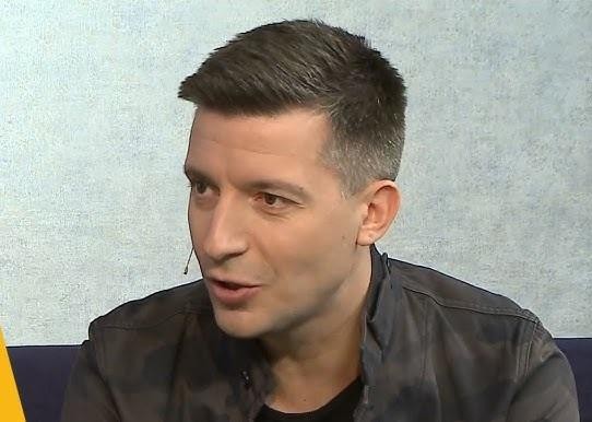 Michał Cessanis trzymający aparat fotograficzny, symbolizujący jego rolę podróżnika i dokumentalisty.