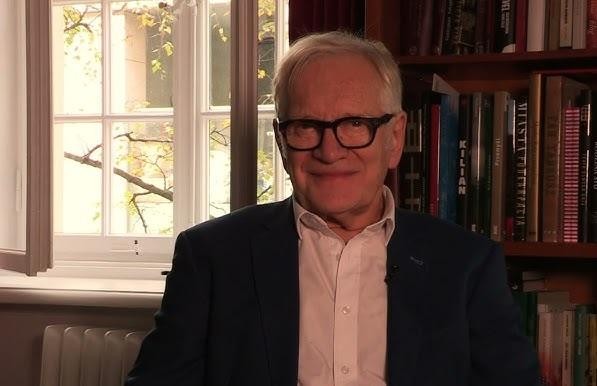 Andrzej Seweryn w dynamicznym ujęciu, w teatralnym otoczeniu, oddający intensywność i zaangażowanie w swoją pracę artystyczną.
