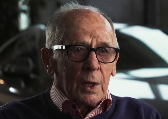 Sobiesław Zasada w klasycznym samochodzie rajdowym (np. Porsche lub BMW) podczas rajdu, oddający dynamikę i ducha epoki jego sportowych sukcesów.