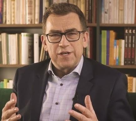 Maciej Orłoś podczas szkolenia z wystąpień publicznych, gestykulujący z energią, w nowoczesnej sali konferencyjnej.