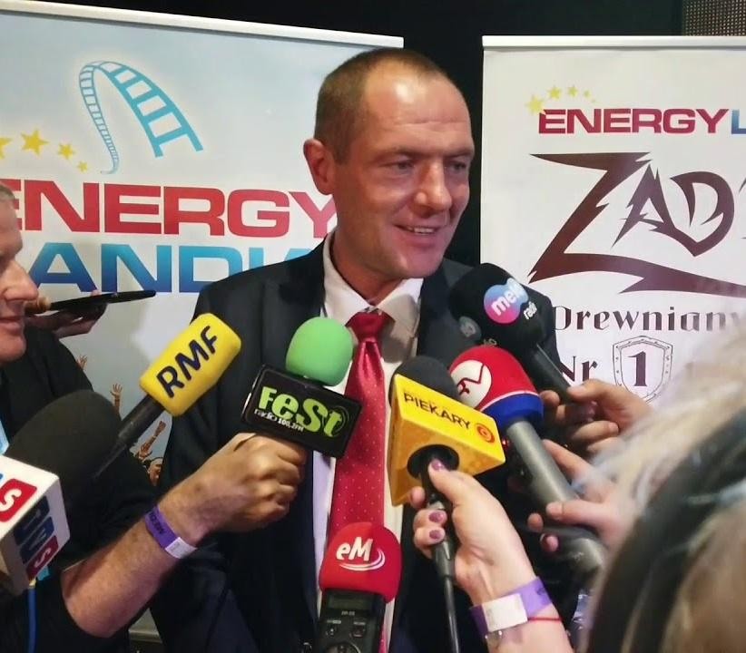 Marek Goczał w kombinezonie rajdowym obok pojazdu SSV na tle pustynnego krajobrazu, symbolizujący jego pasję do rajdów terenowych.