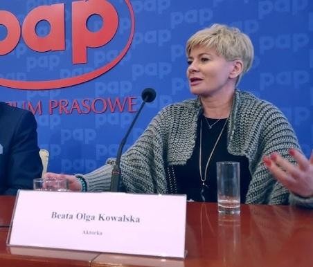 Beata Olga Kowalska w dynamicznej pozie na scenie teatralnej, ubrana w wyrazisty kostium, z dramatycznym oświetleniem podkreślającym jej energię i ekspresję.