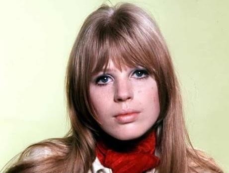 Czarne i białe zdjęcie Marianne Faithfull z końca lat 60. lub początku 70., ukazujące ją w zamyśleniu, być może za kulisami lub w studiu nagraniowym, z elementami muzycznymi w tle.