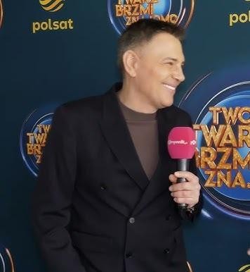 Krzysztof Ibisz przed odrestaurowanym XIX-wiecznym budynkiem na warszawskim Mokotowie, uosabiającym jego miejsce zamieszkania i styl życia.
